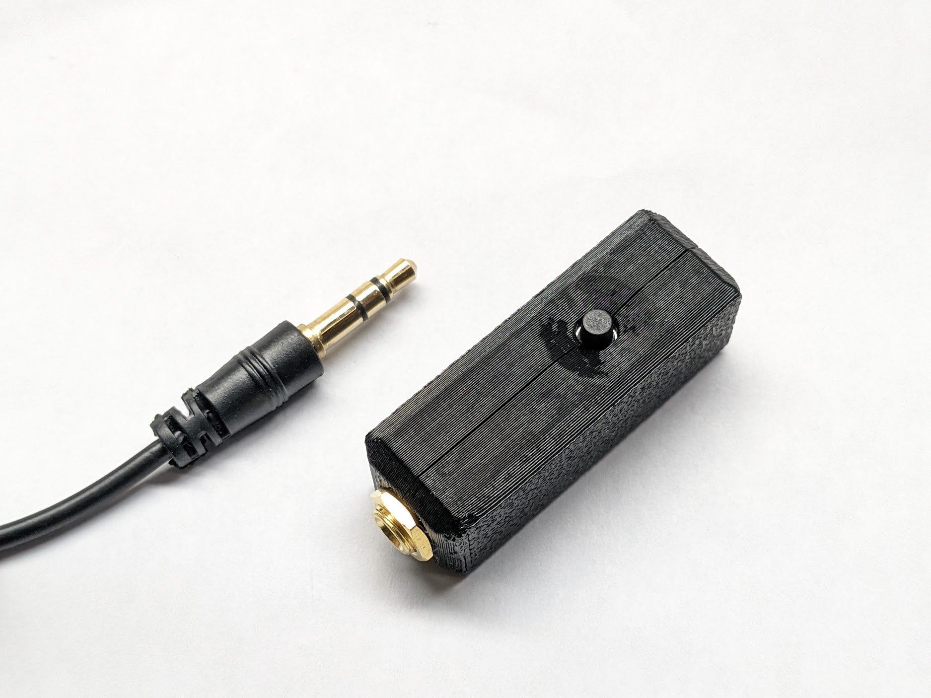 The finished microphone in a black printed case with the push button on top, next to a 3.5mm cable