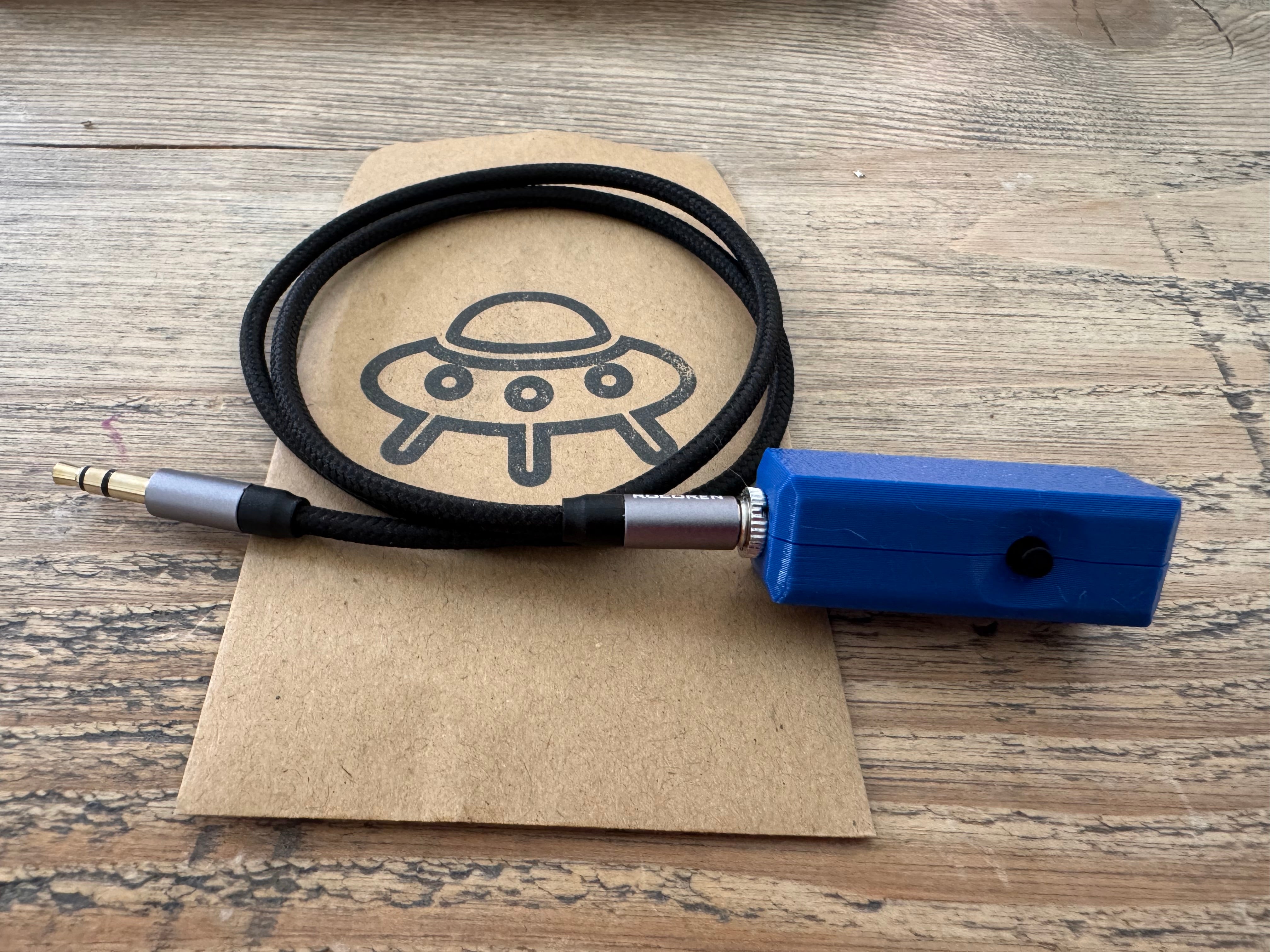 An assembled K6ARK microphone in a blue printed case, with its braided 3.5mm cable coiled on a G7UFO paper bag