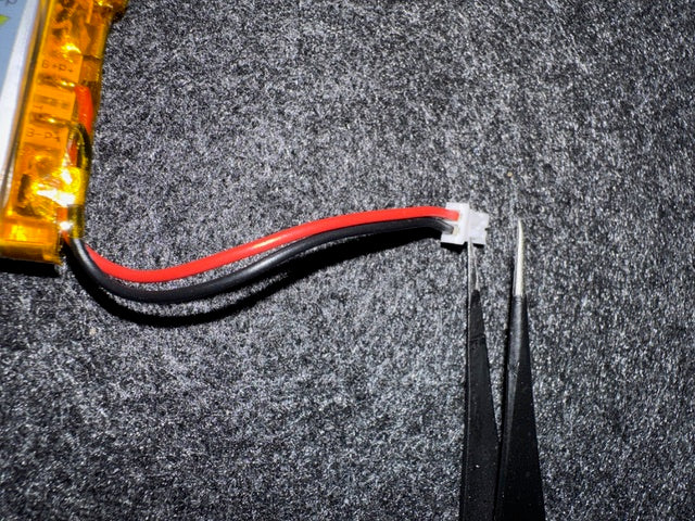 A LiPo battery&rsquo;s JST plug next to a pair of tweezers, with the red and black wires in the opposite positions to those on the battery clip