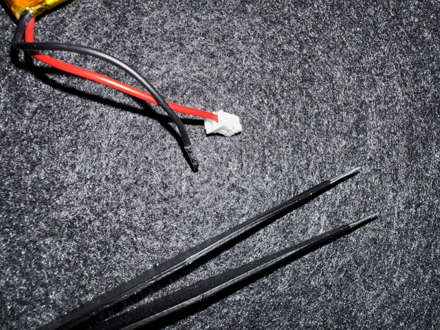The battery&rsquo;s JST plug with the black wire pulled out of its slot, next to a pair of tweezers