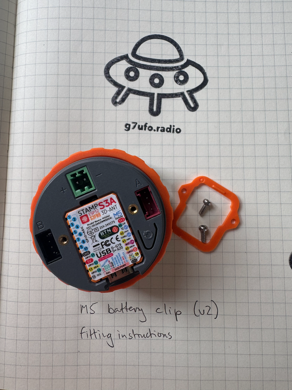 The back of the M5 Dial with the orange back panel clip and its two screws removed, exposing the STAMP S3A board