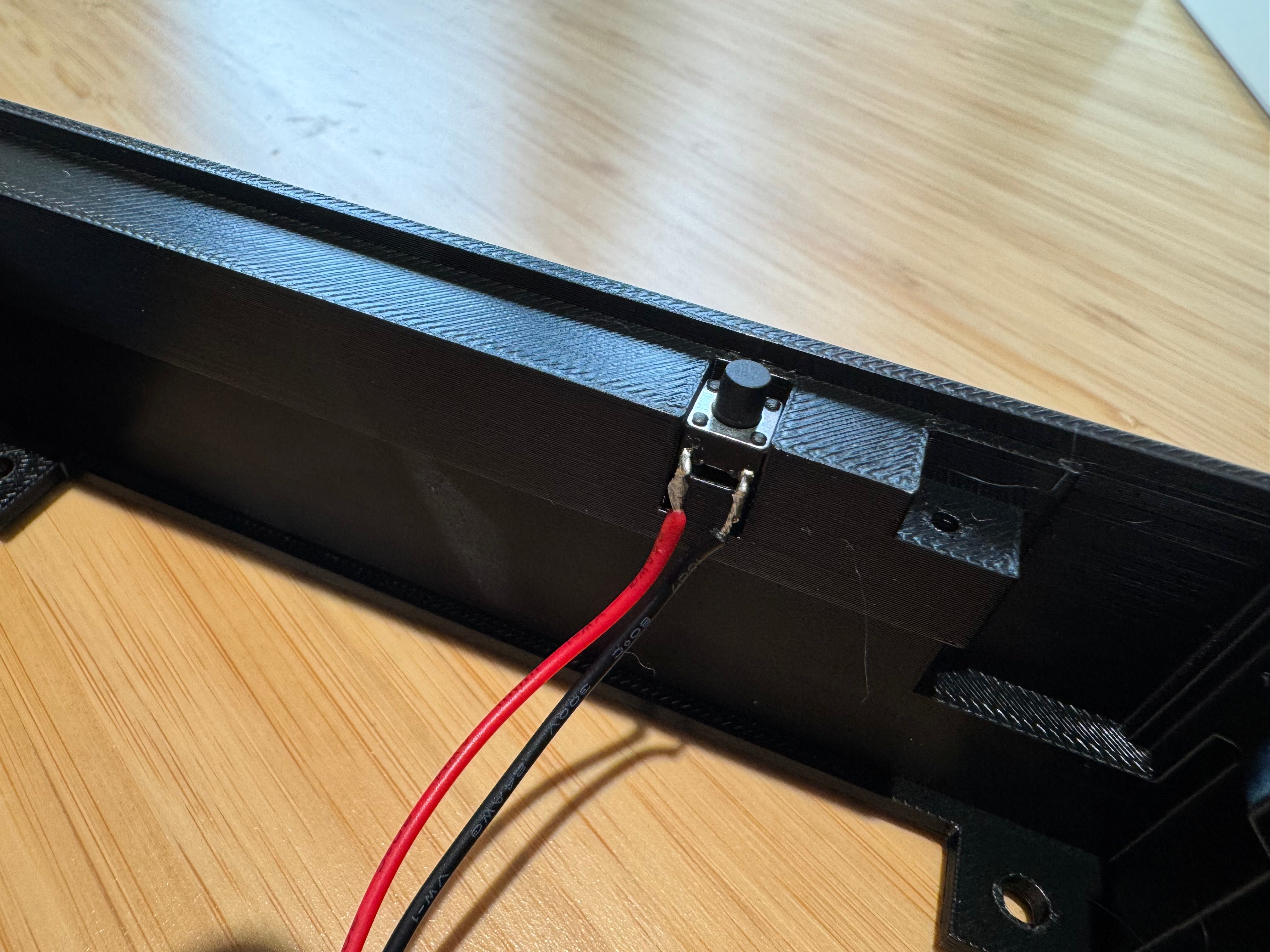 The program button mounted in a slot on the inside wall of the case, with its red and black wires hanging down
